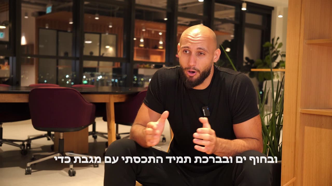 Dennis talking to camera in a warm-lit lounge, with Hebrew subtitles